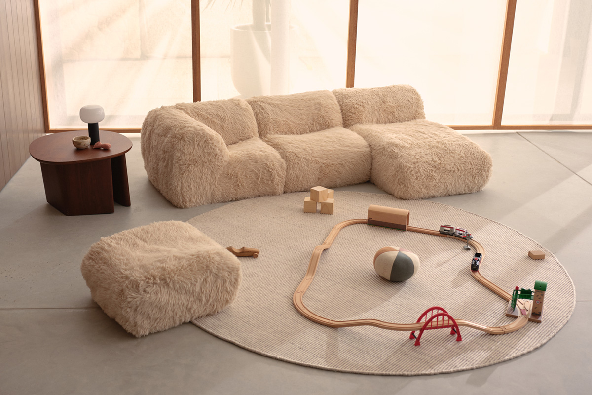 A neutral-toned kids playroom decorated with a fluffy sofa, timber table and a beige round rug with a train track.