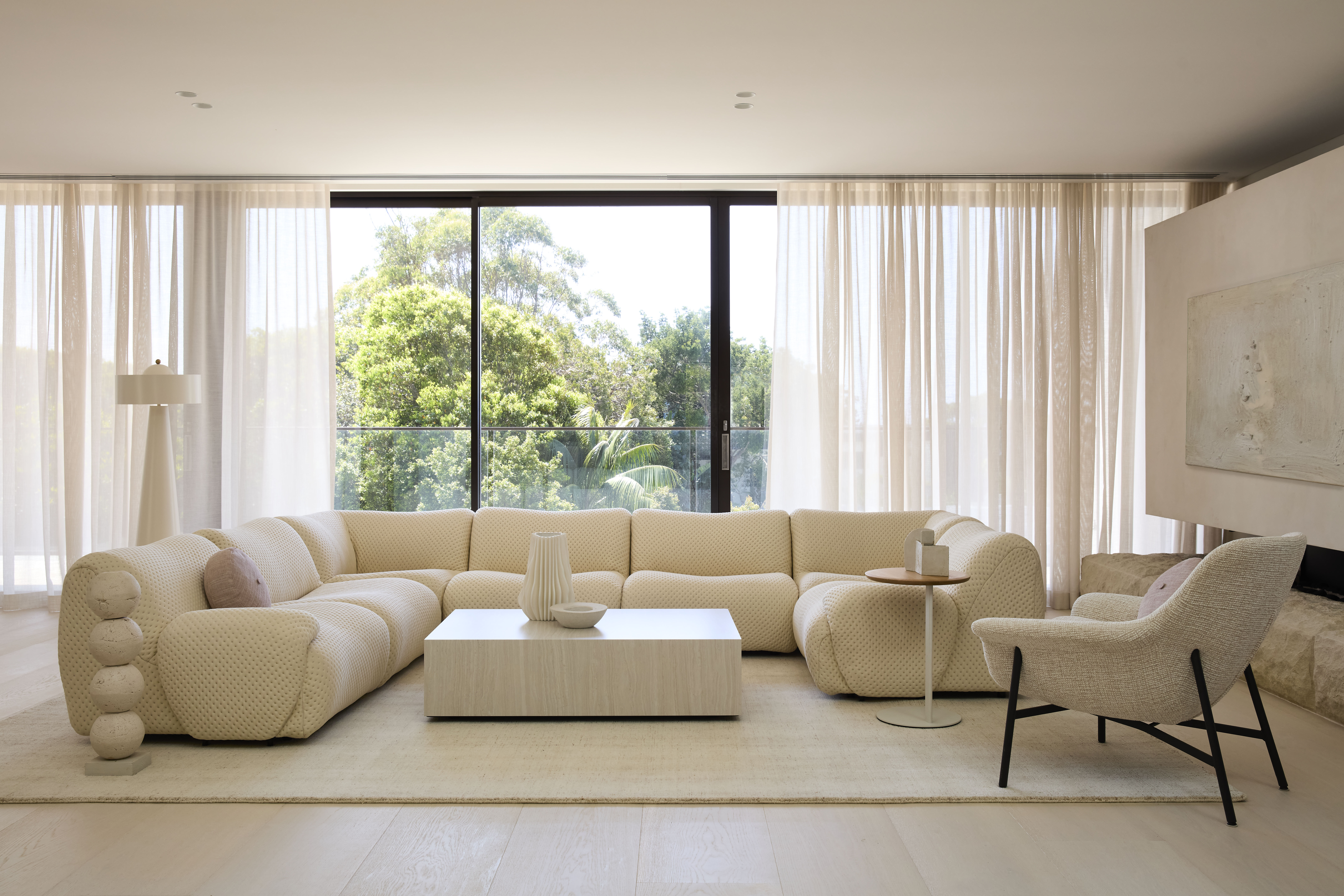 A wide shot of Lara Hutton’s light-filled modern living space, framed by outdoor greenery and featuring a curved modular sofa with complementary King Living accents.