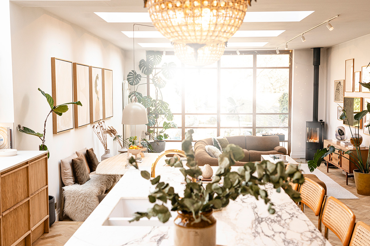 Bright, open plan living and dining space featuring a marble island, natural textures and a curved caramel bouclé sofa, paired with warm neutrals and greenery.