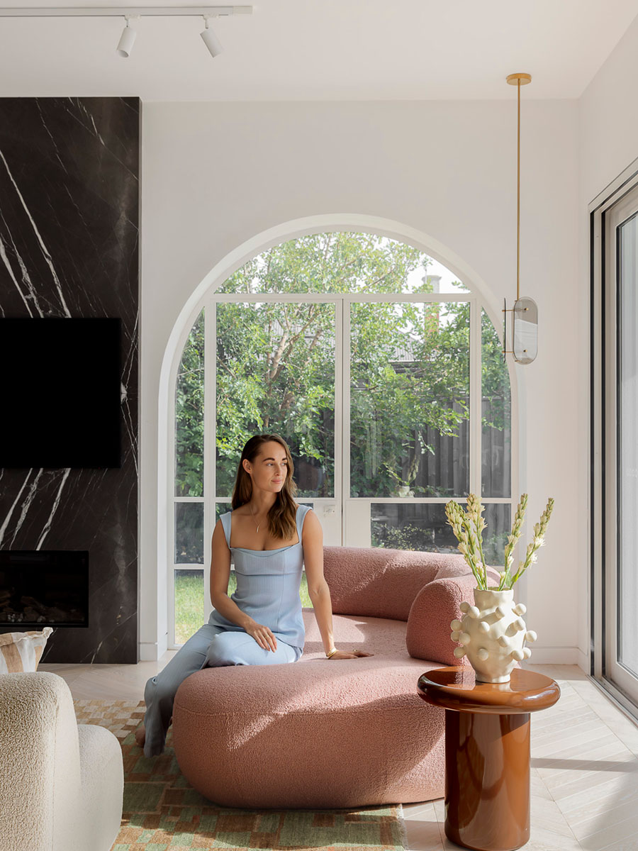 A light-filled contemporary living space with a curved, rose-toned sofa, sculptural side table and patterned rug.
