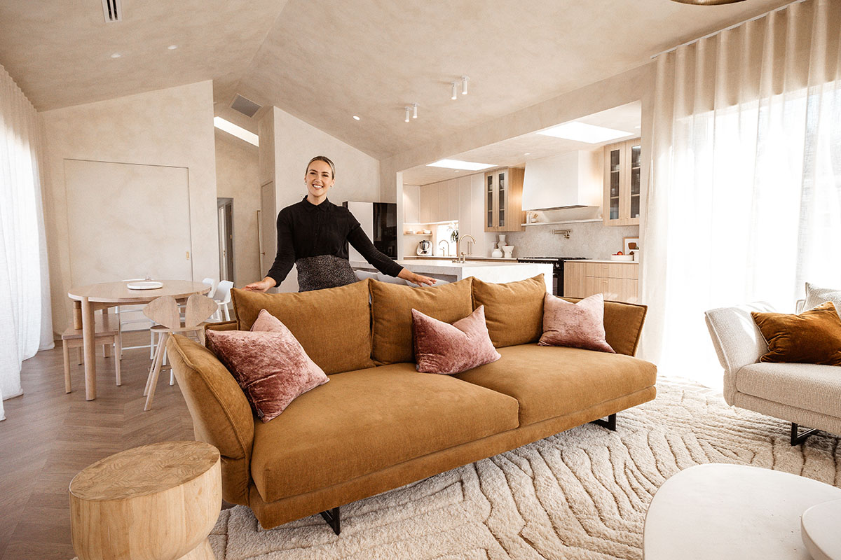 Interior Stylist and Content Creator Sarah Pickersgill-Brown stands with a tobacco-toned, velvet sofa in an open-plan living and dining space.